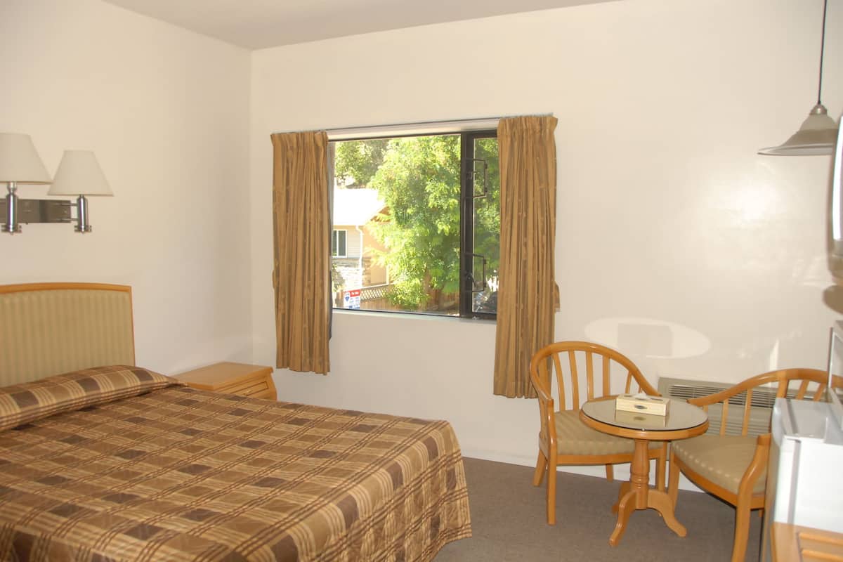 A hotel room with a bed, a chair, a small table, and a window with curtains.