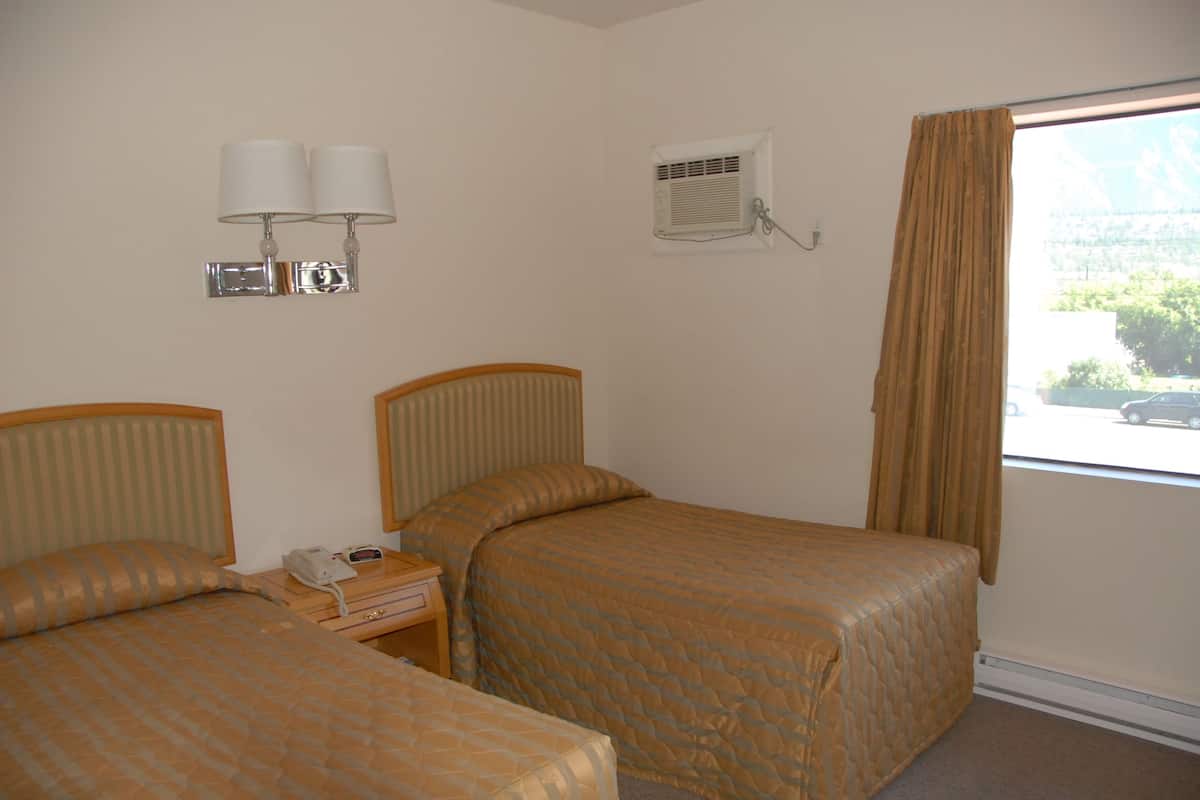 A hotel room with two beds, a nightstand with a phone, wall-mounted lamps, an air conditioning unit, and a window with curtains.