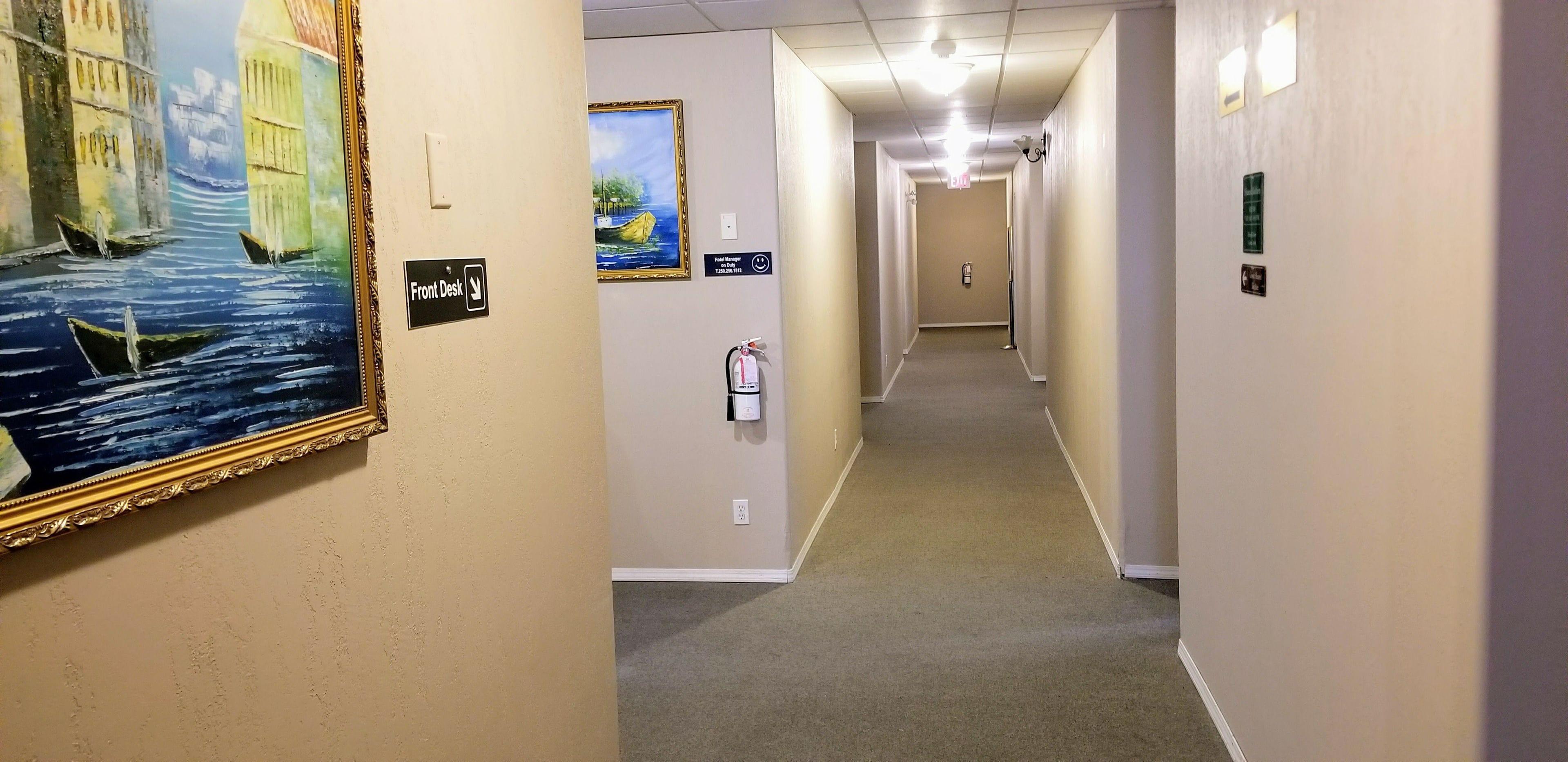 Un couloir d’hôtel orné d’un tableau représentant un paysage fluvial, avec un extincteur et un panneau indiquant l’emplacement de la réception.