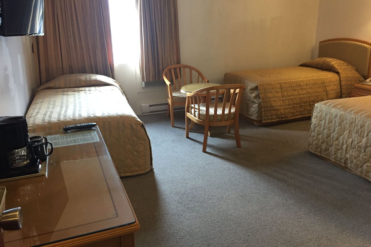A hotel room with two beds, a desk, a chair, and a TV.