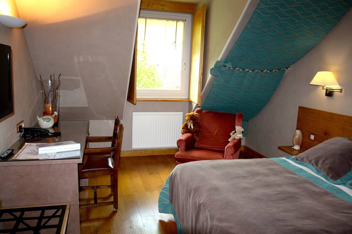 A hotel room with a bed, a desk with a lamp, a chair, and a window.