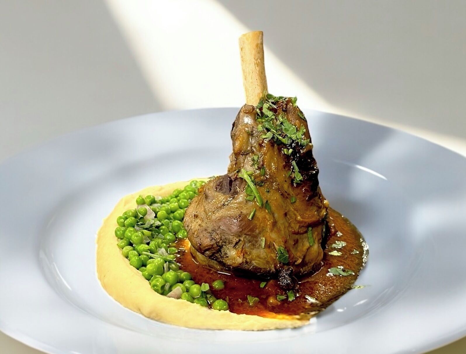 A plate with a lamb shank, peas, and a sauce.