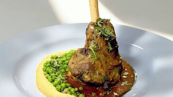 A plate with a lamb shank, peas, and a sauce.