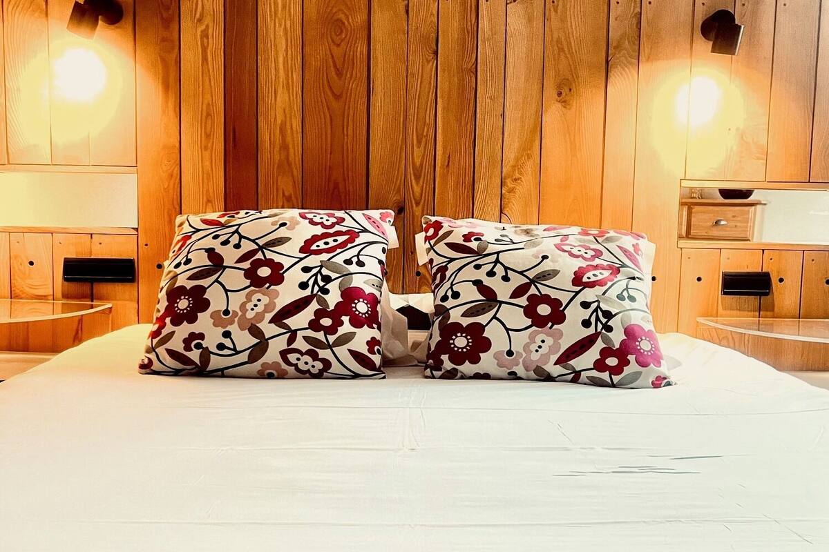 A bed with floral-patterned pillows and wooden paneling on the walls.