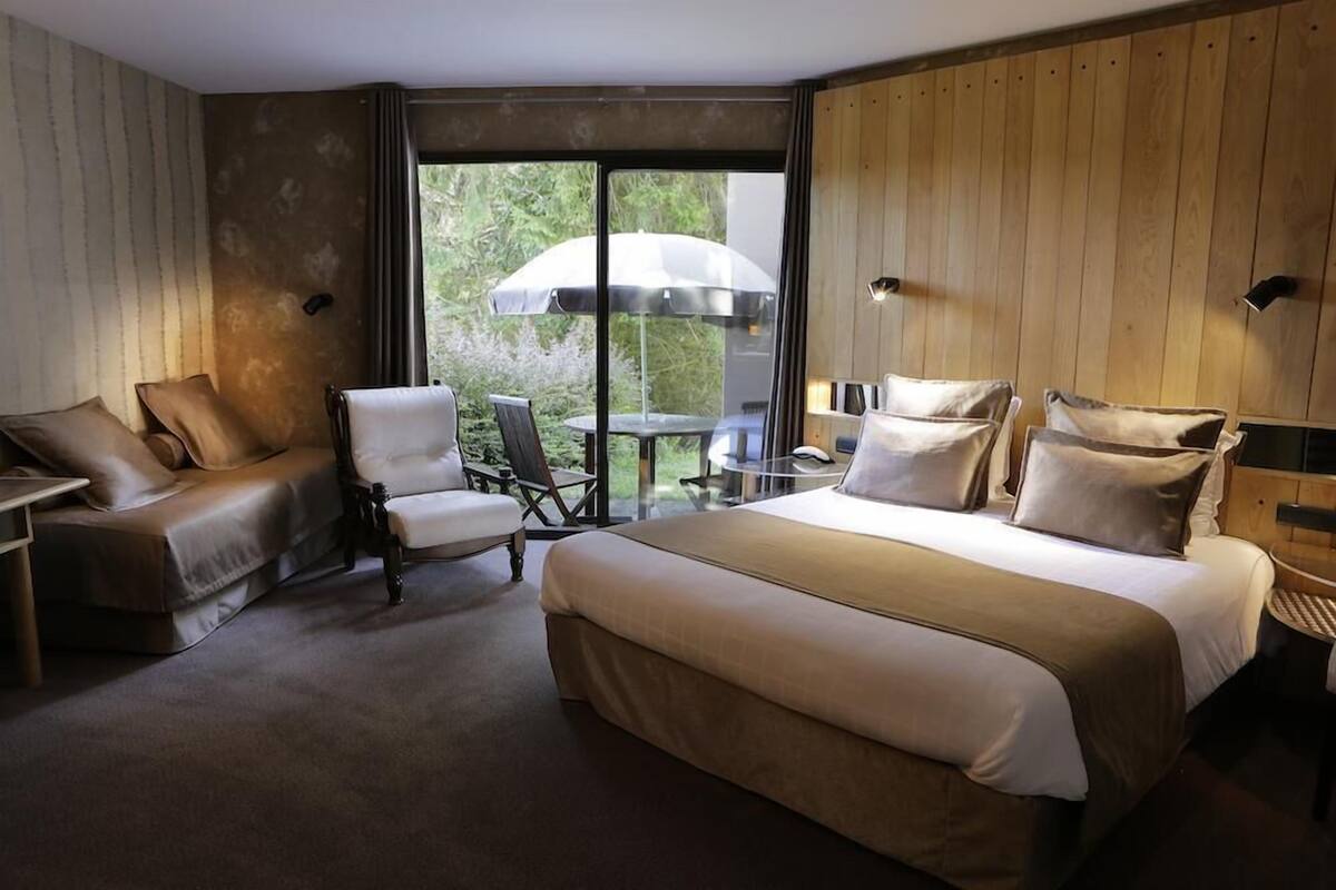 A hotel room with a large bed, a sofa, a chair, and a table with an umbrella.