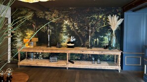 Una barra de madera con diseño rústico, que incluye una lámpara de araña, jarrones decorativos y un mural con un bosque de fondo.