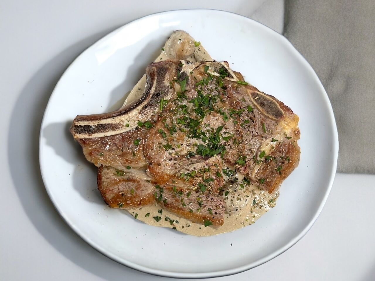 Un plato blanco con un filete a la parrilla cubierto de hierbas y salsa cremosa.