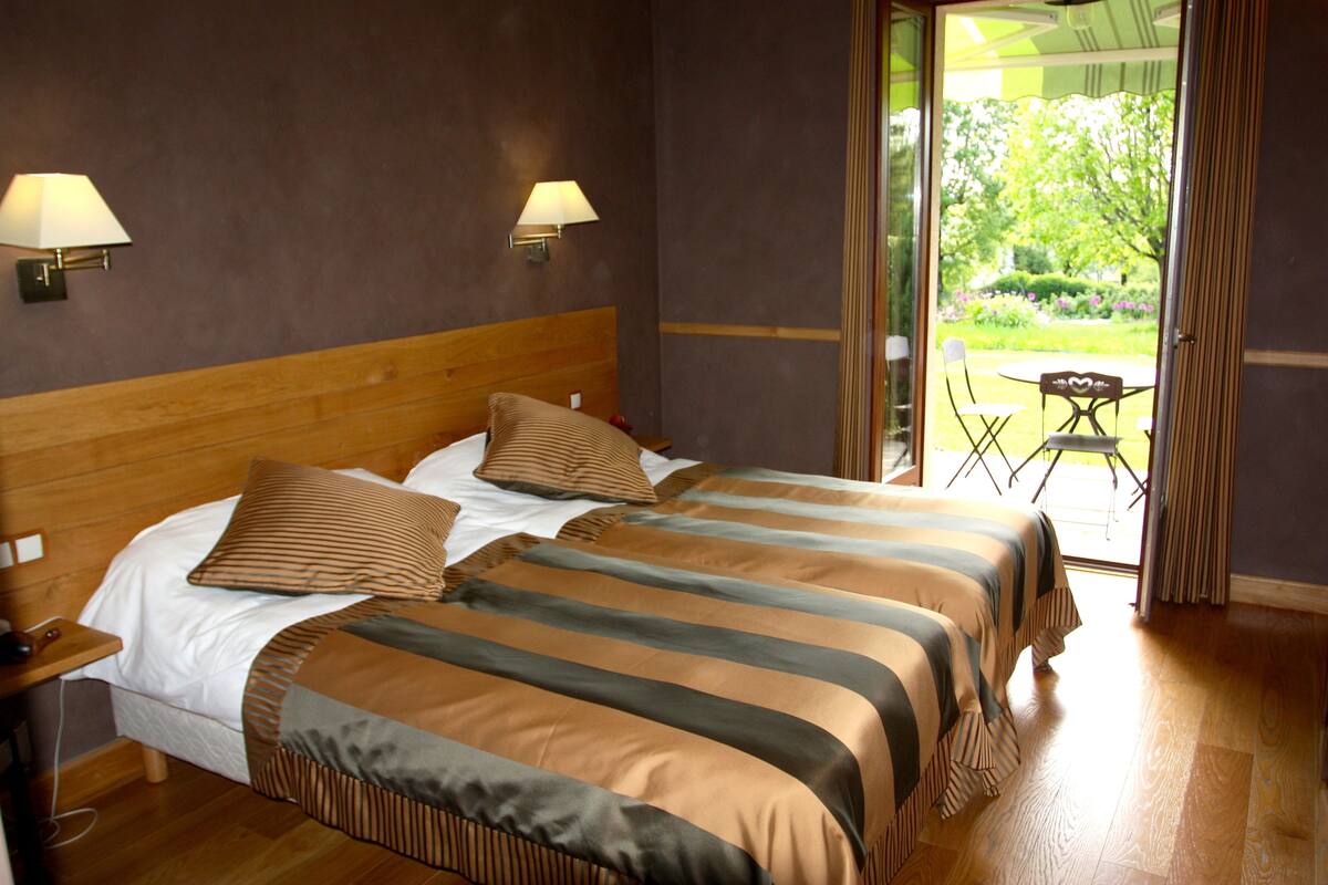A hotel room with two beds, a wooden headboard, two bedside lamps, and a view of a garden through a glass door.