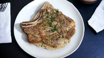 A plate of steak with a creamy sauce and herbs, served on a white plate.