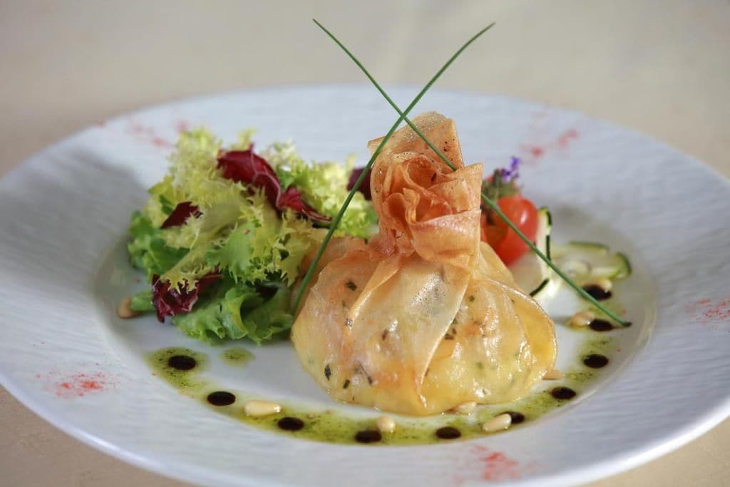 A plate with a rolled pastry, a salad, and a garnish.