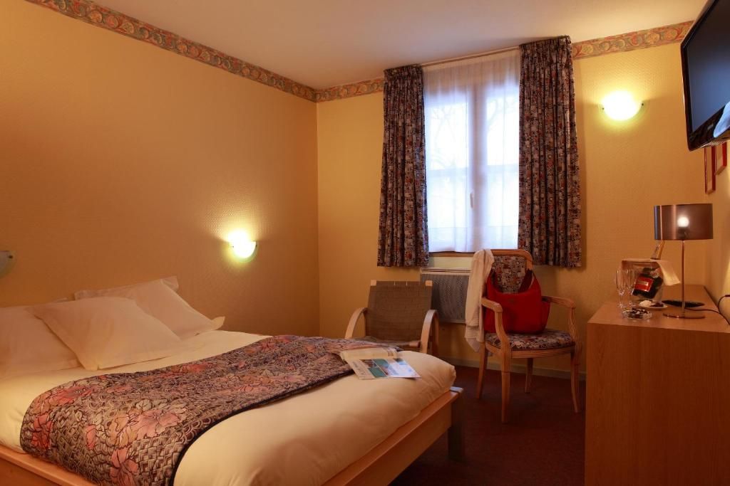 A hotel room with a bed, a desk, a chair, a television, and a window with curtains.