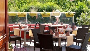 An outdoor patio with tables and chairs, a striped awning, and potted plants. - Le Luth (Mirecourt)