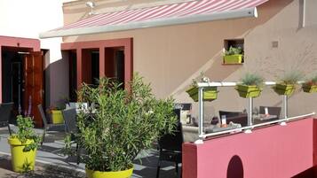 An outdoor seating area with yellow planters, a red awning, and a building with a beige facade.