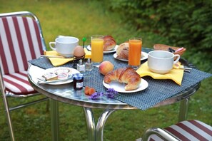 An outdoor breakfast setup with a table, chairs, and a variety of food items including croissants, eggs, and juice. - Le Luth (Mirecourt)