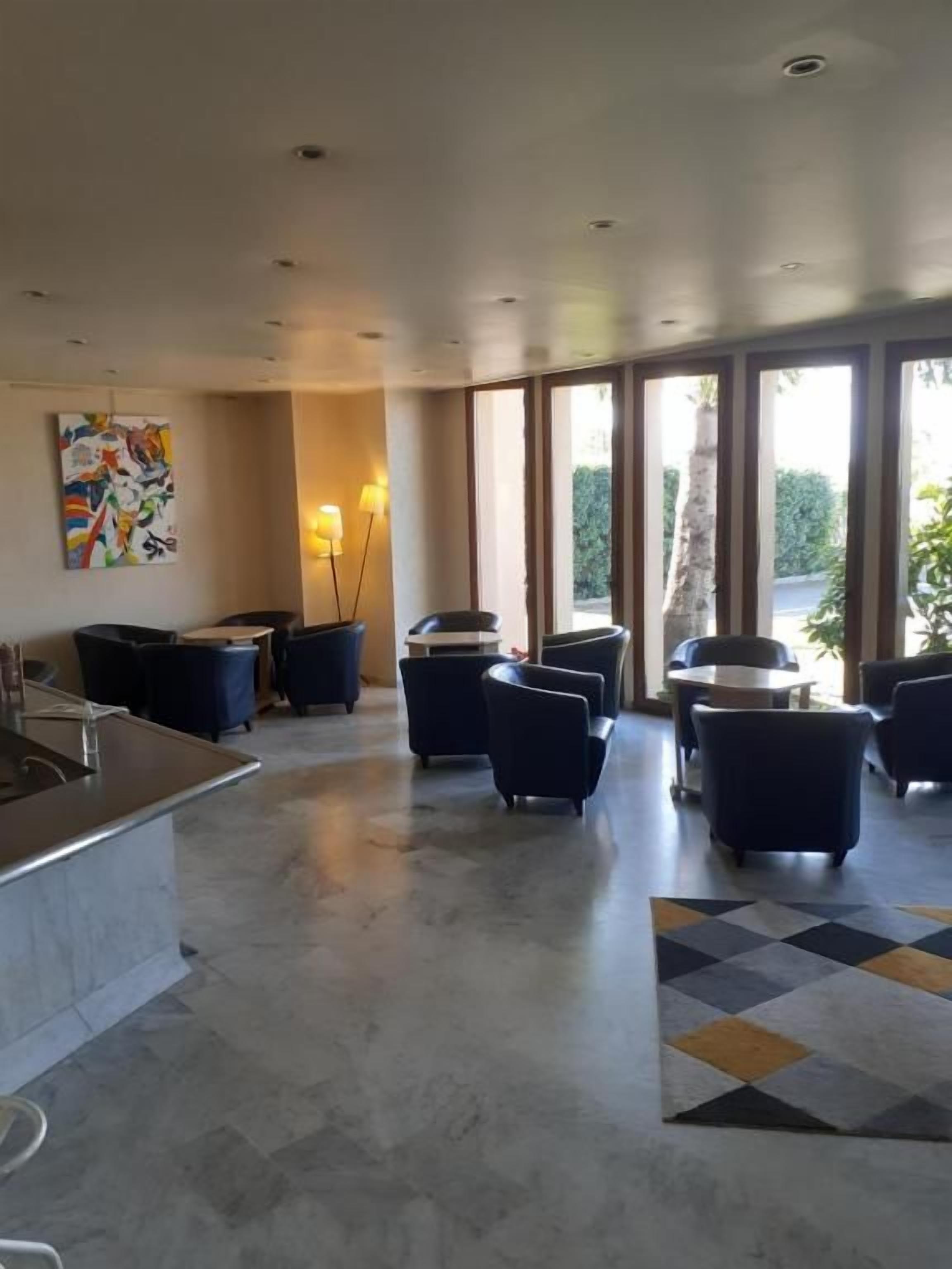 Eine großzügige Lobby mit Marmorboden, einer zentralen Sitzecke mit Sofas, einem kleinen Tisch und einem großen Fenster mit Blick auf Grünflächen.