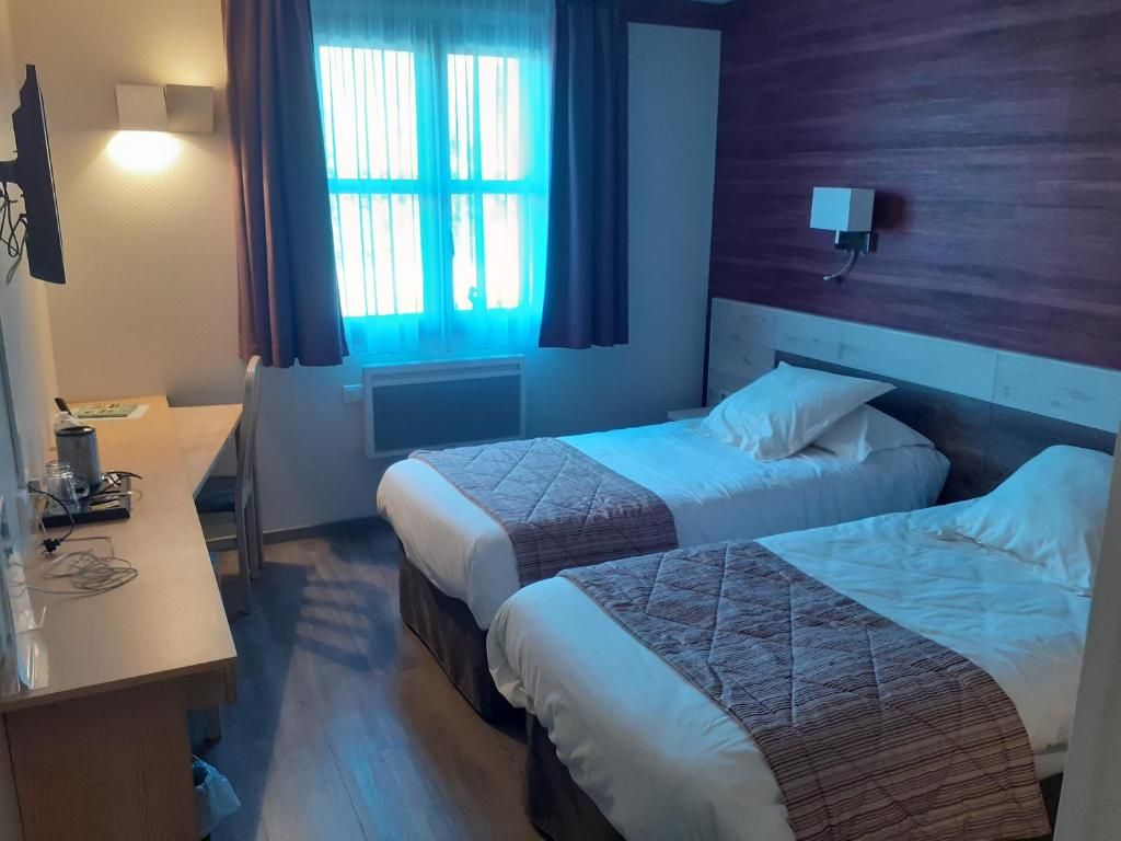 Habitación de hotel con dos camas, un escritorio, una silla y una ventana con cortinas.
