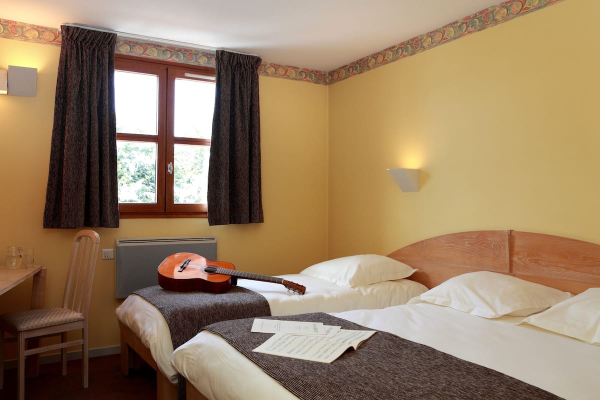 A room with two beds, a guitar, a chair, and a desk.