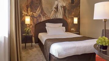 A hotel room with a large bed, a headboard, two bedside tables with lamps, a small potted plant, and a large wall painting.