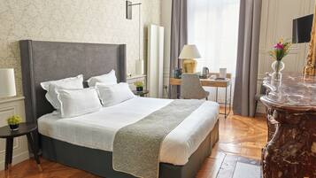 A hotel room with a large bed, a desk with a lamp, a TV, and a vase with flowers.