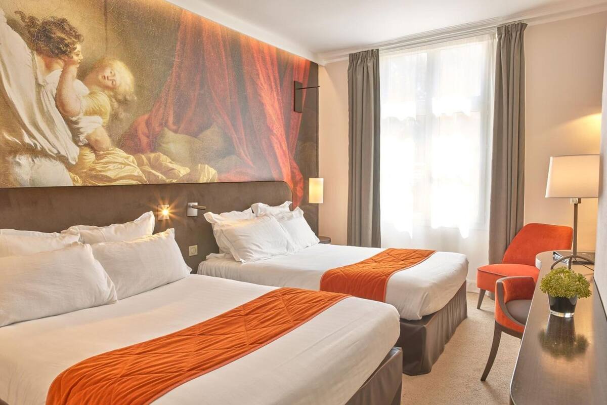 A hotel room with two beds, a large painting on the wall, a desk with a lamp, and a chair.