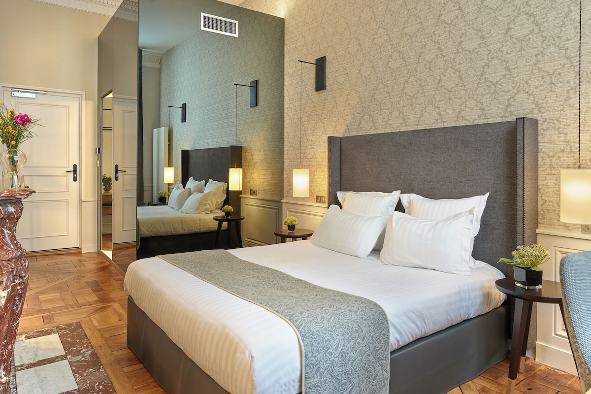 A modern hotel room with a large bed, a mirror, bedside tables, and a view of the hallway.