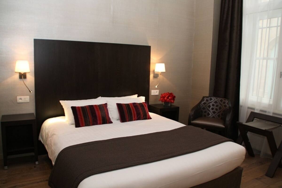 A hotel room with a large bed, two bedside tables, a chair, and a window with curtains.