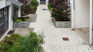 A narrow cobblestone courtyard with white buildings, a central door, and small gardens. - Hotel De Guise (Nancy)