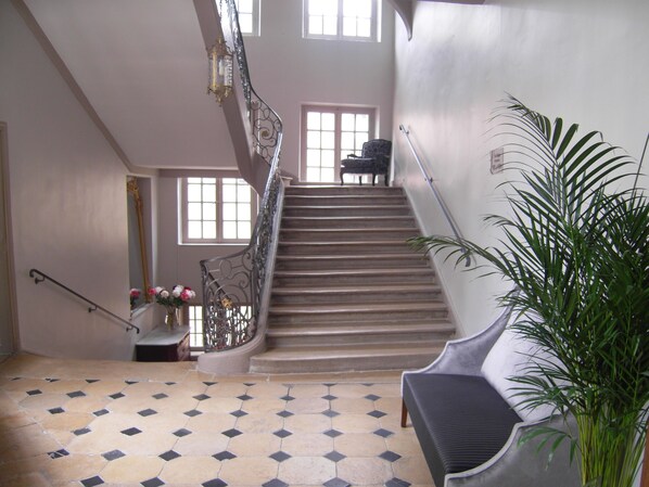 A grand staircase with a metal railing, a potted plant, and a chair.