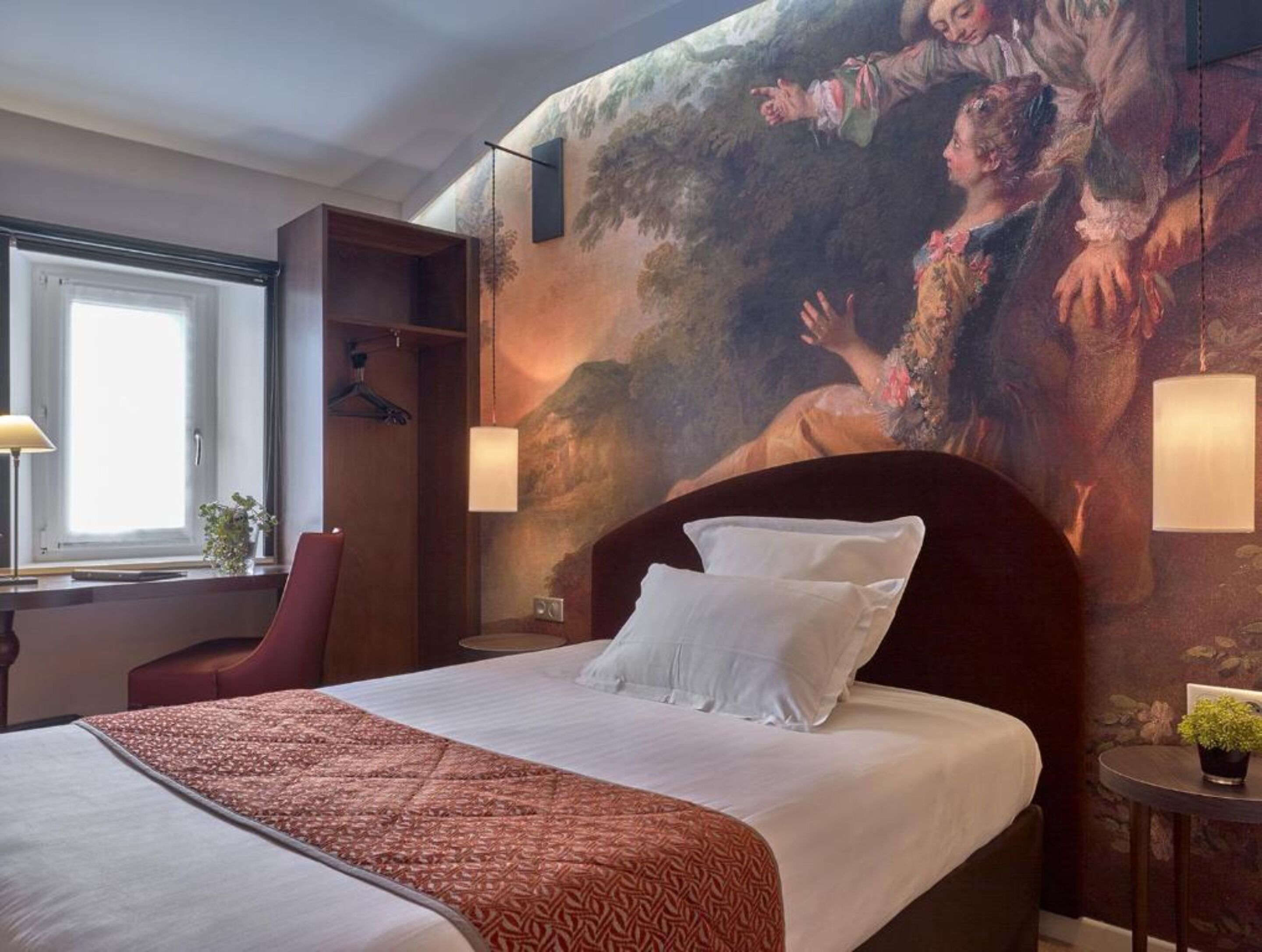 Quarto de hotel com uma cama grande, uma escrivaninha com abajur, uma cadeira e um quadro na parede.