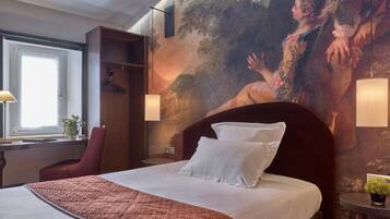 A hotel room with a large bed, a desk with a lamp, a chair, and a painting on the wall.