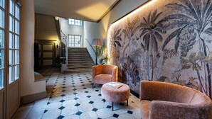 A lobby with a staircase, two armchairs, a patterned wall, and a tiled floor. - Hotel De Guise (Nancy)