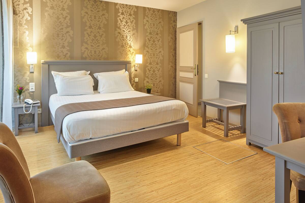 A hotel room with a large bed, bedside lamps, a wooden floor, a desk, and a wardrobe.