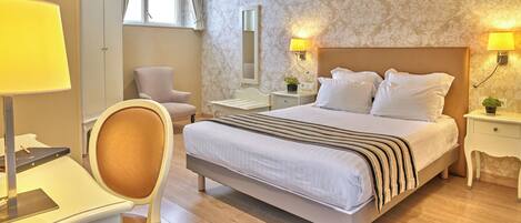 A hotel room with a large bed, two bedside lamps, a desk with a chair, a wardrobe, and a window with curtains.