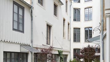 A narrow cobblestone pathway between buildings with white facades and multiple windows.