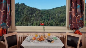 A dining table with breakfast items, a vase with a flower, and a view of a forested mountain. - Hotel De la Grande Cascade (Le Tholy)