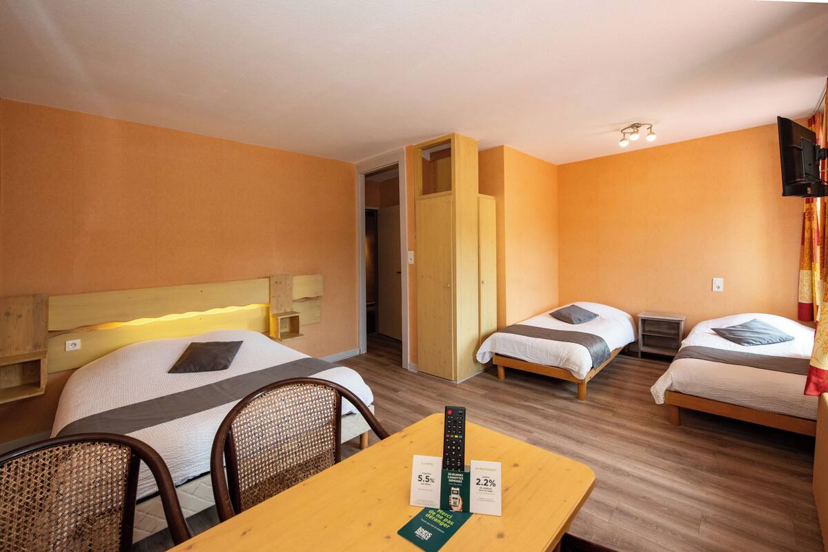 Habitación de hotel con dos camas individuales, un cabecero de madera, una mesita con un control remoto y una silla.