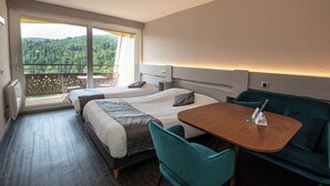 A hotel room with two beds, a balcony with a view, a dining table, and teal chairs. - Hotel De la Grande Cascade (Le Tholy)