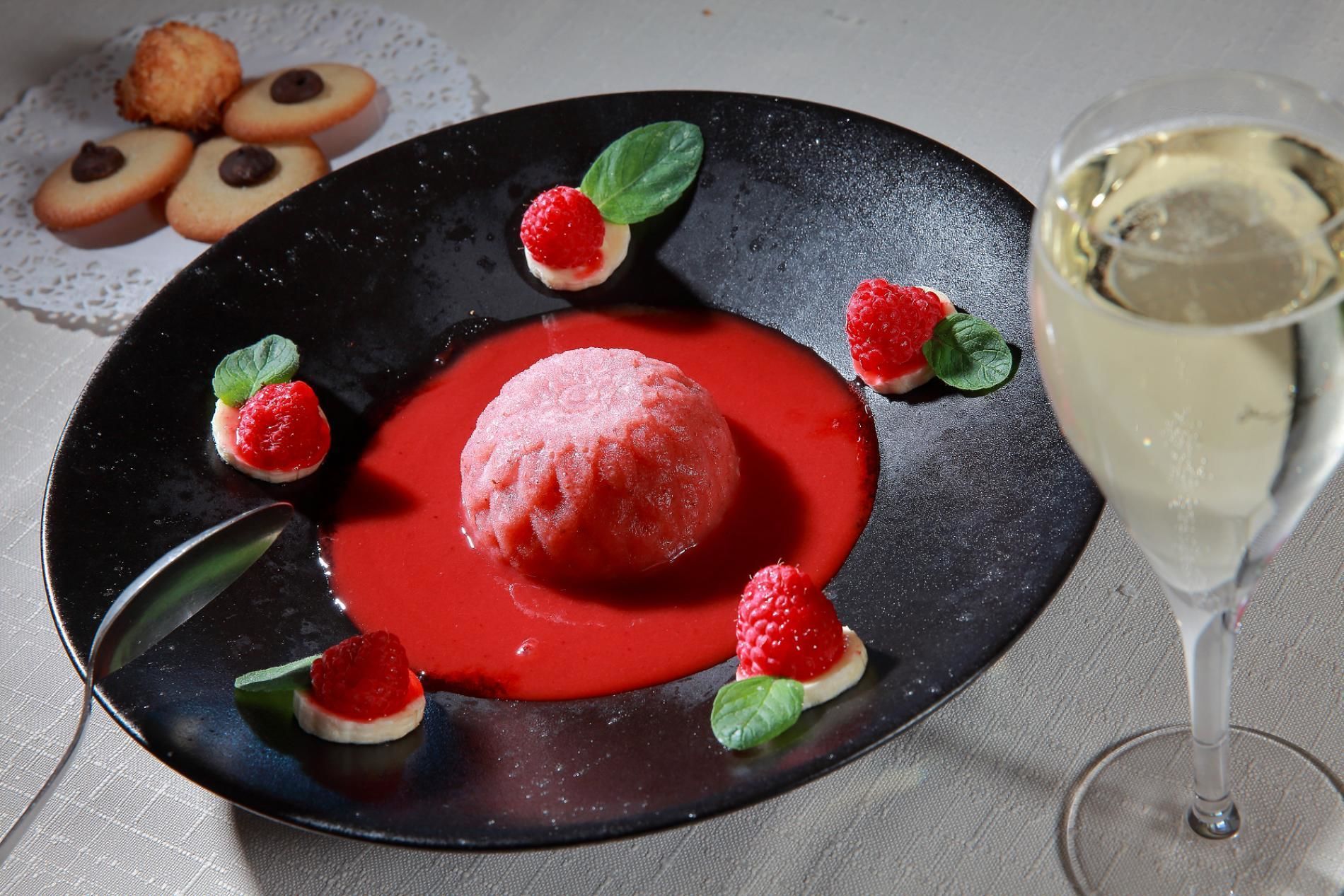 A dessert plate with a red dessert, strawberries, and mint leaves.