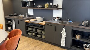 A modern kitchen with grey cabinets, a microwave, a toaster, and a wooden dining table with orange chairs. - Hotel De la Grande Cascade (Le Tholy)
