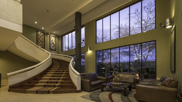 A spacious lobby with a curved staircase, leather sofas, and large windows offering a view of the outdoors.