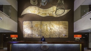 A reception desk with a receptionist, a large wall mural, and a modern chandelier.