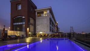 A modern hotel with a swimming pool, outdoor seating, and a large glass facade.