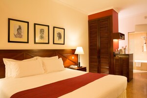 Habitación de hotel con una cama grande, una mesita de noche, una lámpara y tres cuadros en la pared.
