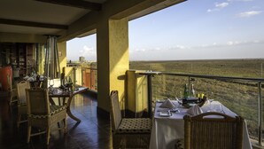 A dining area with wicker chairs and a table set for two, overlooking a vast landscape.