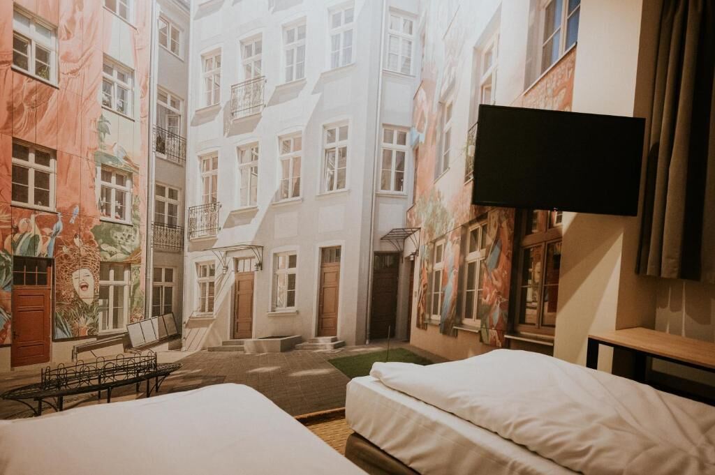 Habitación de hotel con cama, televisor y vista a una calle estrecha flanqueada por edificios.