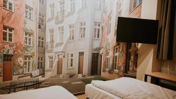 Habitación de hotel con cama, televisor y vista a una calle estrecha flanqueada por edificios.