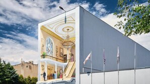 A building with a large mural of a grand interior, a staircase, and flags on the side.