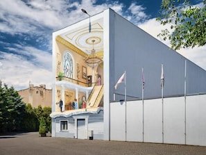 A building with a large mural of a grand interior, a staircase, and flags on the side. - Iness Hotel (Łódź)