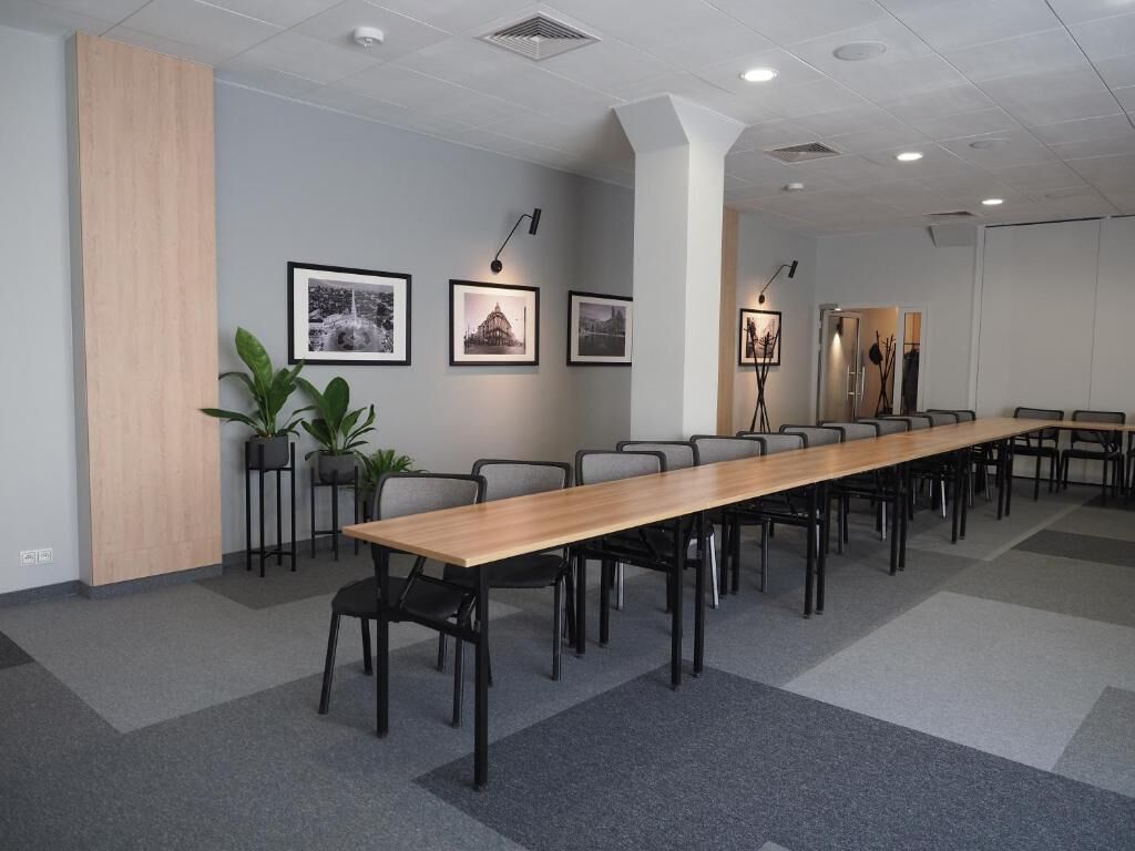 Un salón de conferencias con una larga mesa, sillas, cuadros en la pared y plantas en macetas.