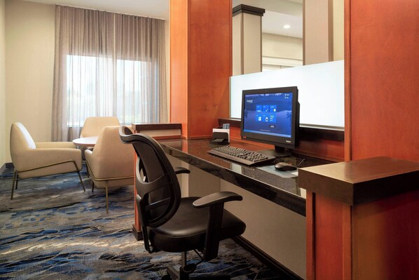 Habitación de hotel con escritorio, computadora, dos sillas, un ventanal con cortinas y piso alfombrado.